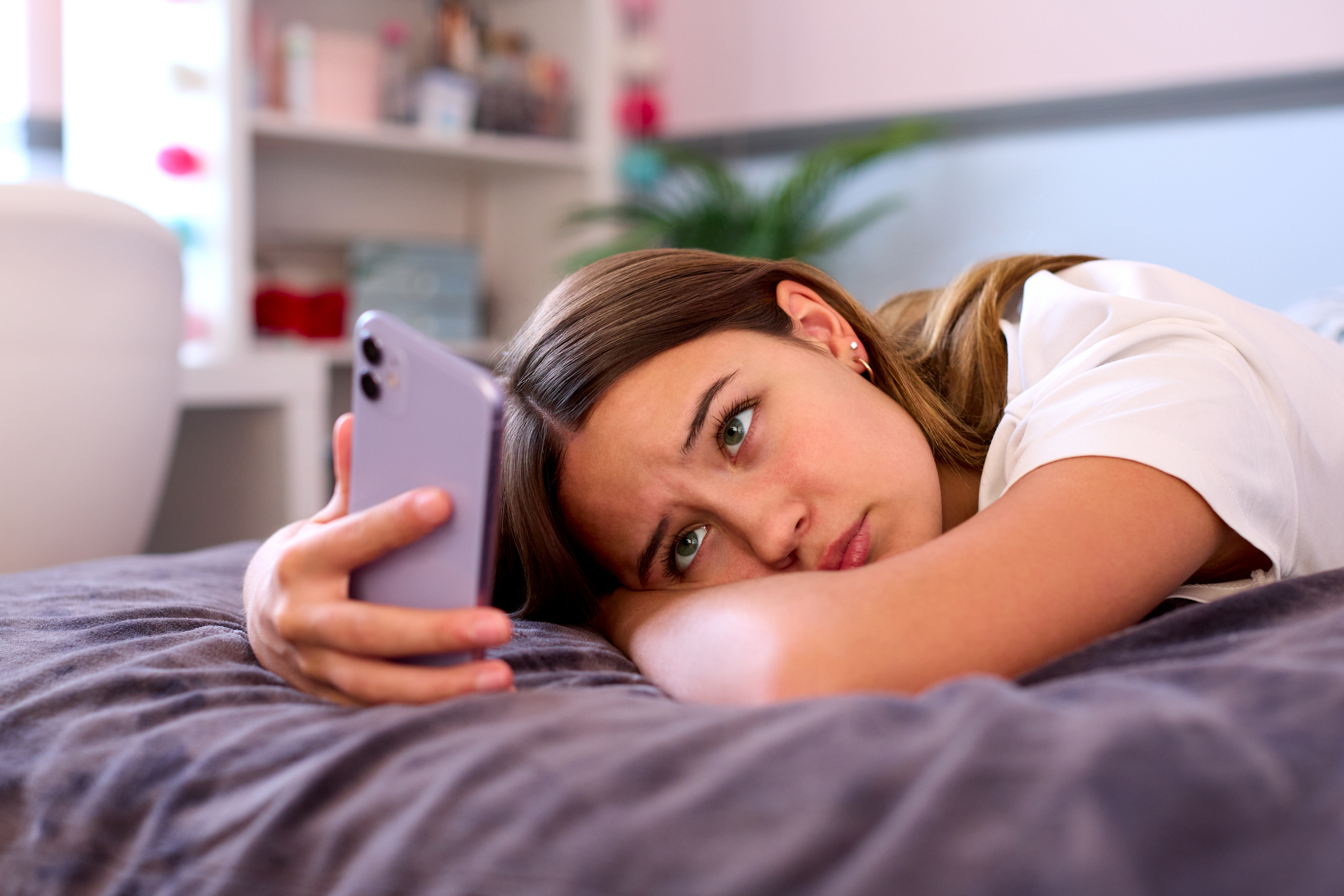 Young woman lying on her bed staring at her phone, feeling disconnected